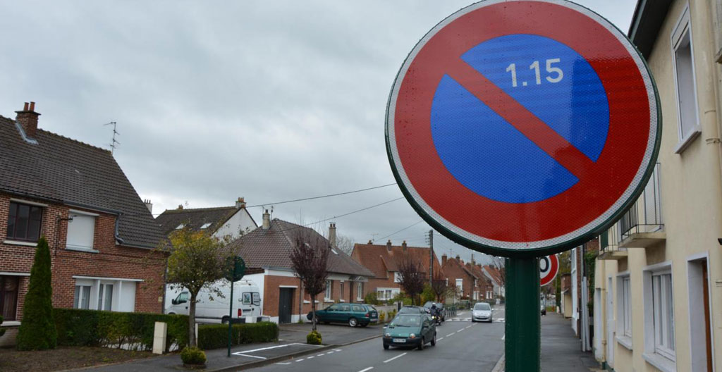 Gros plan sur un panneau B6a stationnement interdit fixé sur un poteau métallique avec une note administrative municipale partiellement visible